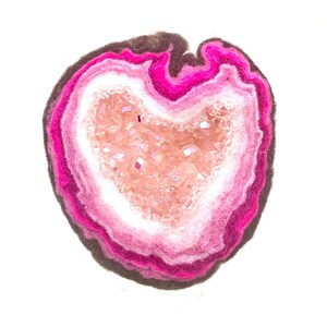 May include: A pink and white felt geode with a crystal-like center. The geode is made of layers of felt, with the outer layer being a dark pink and the inner layer being a light pink. The center of the geode is filled with small, white crystals.