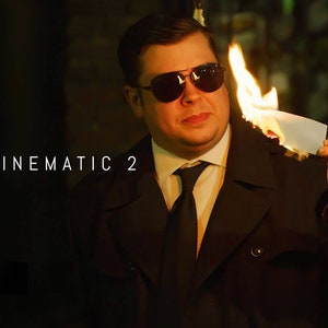 May include: A man in a black suit and sunglasses holds a piece of paper on fire. The text "MTITLE CINEMATIC 2" is visible in the background.