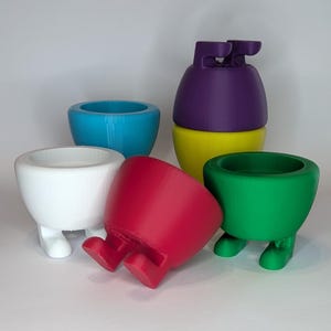 May include: Five 3D printed egg cups in different colors: white, blue, red, green, and purple. The purple egg cup is stacked on top of a yellow egg cup.