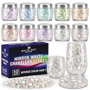 May include: Ten small glass jars with silver lids containing iridescent flakes in various colors, a dark blue box labeled BALTIC DAY MIRROR WHITE CHAMELEON FLAKES, two clear glass tumblers, and a circular coaster filled with the flakes.