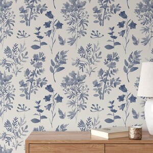K&ouml;nnte beinhalten: Eine wei&szlig;e Wand mit einer blauen floralen Tapetenmuster. Ein Holztisch mit einer Lampe, einem Buch und einer Kerze darauf.