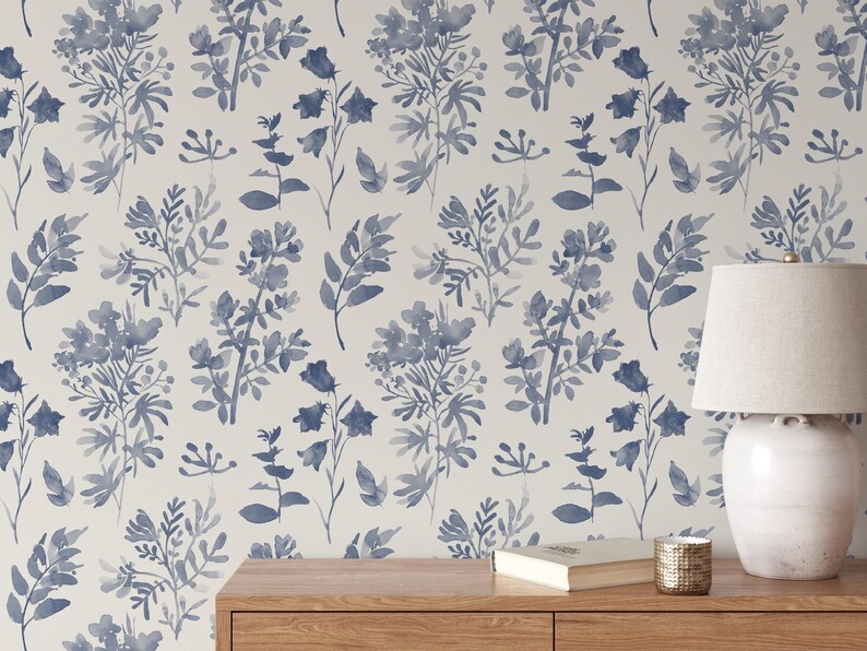K&ouml;nnte beinhalten: Eine wei&szlig;e Wand mit einer blauen floralen Tapetenmuster. Ein Holztisch mit einer Lampe, einem Buch und einer Kerze darauf.
