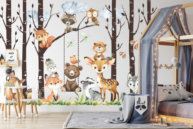 May include: A white wall with a brown tree mural featuring a variety of woodland animals, including a deer, a bear, a raccoon, a fox, a squirrel, an owl, and a beaver. The mural is decorated with butterflies and dragonflies. The wall is in a nursery with a wooden bed and a white chair.