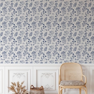 K&ouml;nnte beinhalten: Eine wei&szlig;e Wand mit einem blauen floralen Tapetenmuster. Ein Korbstuhl mit einem hellblauen Kissen steht vor der Wand. Zwei Korbwaren stehen auf dem Boden vor dem Stuhl.