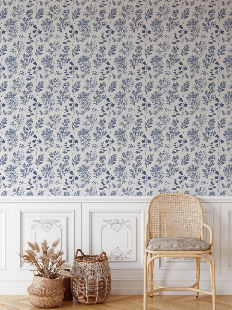 K&ouml;nnte beinhalten: Eine wei&szlig;e Wand mit einem blauen floralen Tapetenmuster. Ein Korbstuhl mit einem hellblauen Kissen steht vor der Wand. Zwei Korbwaren stehen auf dem Boden vor dem Stuhl.