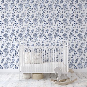 K&ouml;nnte beinhalten: Ein wei&szlig;es Babybett mit einer wei&szlig;en Matratze und einem wei&szlig;en Kissen mit dem Text "Gute Nacht" darauf. Das Babybett steht vor einer Wand mit einer blauen und wei&szlig;en floralen Tapetenmuster.