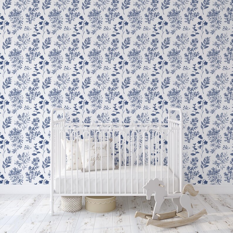 K&ouml;nnte beinhalten: Ein wei&szlig;es Babybett mit einer wei&szlig;en Matratze und einem wei&szlig;en Kissen mit dem Text "Gute Nacht" darauf. Das Babybett steht vor einer Wand mit einer blauen und wei&szlig;en floralen Tapetenmuster.