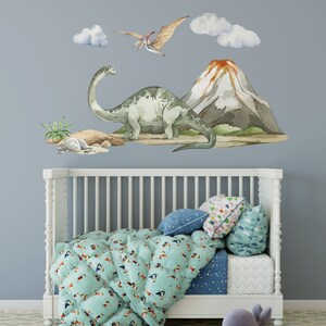 May include: A white crib with a blue and green patterned comforter and pillows. The wall behind the crib has a watercolor dinosaur and volcano scene with clouds.