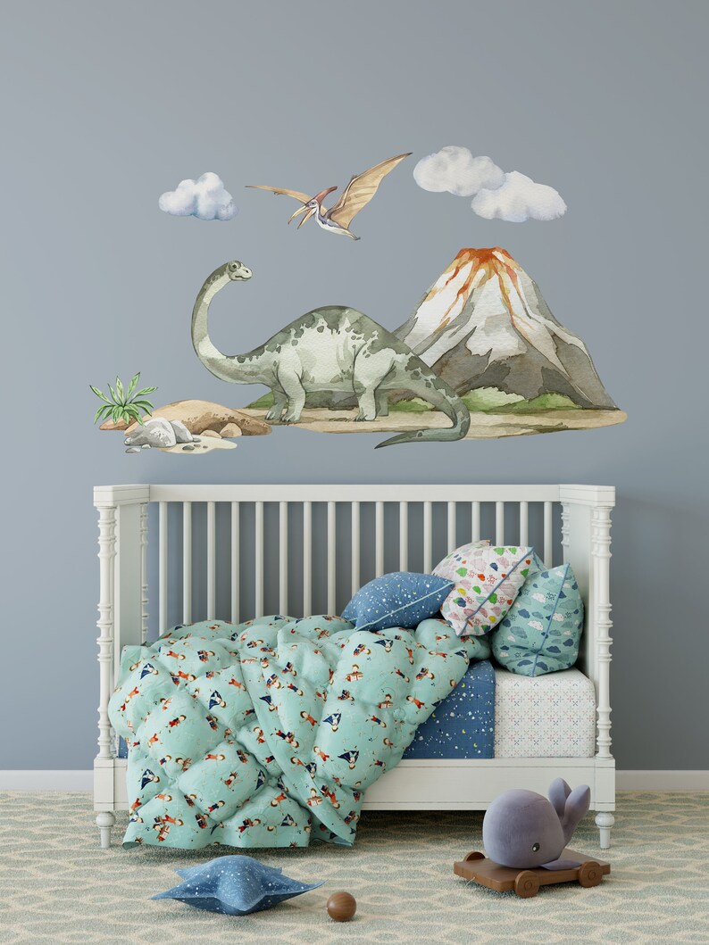 May include: A white crib with a blue and green patterned comforter and pillows. The wall behind the crib has a watercolor dinosaur and volcano scene with clouds.