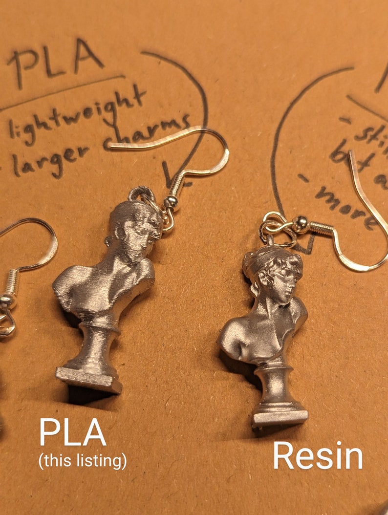 This photo shows a closeup of a plastic PLA Sappho Bust earring next to a resin Sappho Bust earring.