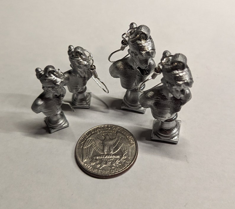This photo shows two pairs of Sappho bust earrings - one dainty size and one statement size - next to a quarter for scale. All of the items are set against a white background.