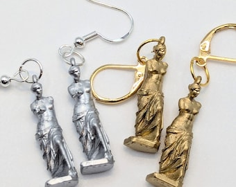 May include: A pair of silver and gold earrings featuring miniature sculptures of the Venus de Milo. The earrings have a hook closure.
