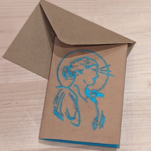 May include: A brown card with a blue outline of a woman's face with a halo around her head. The card is folded in half and has a brown envelope behind it.