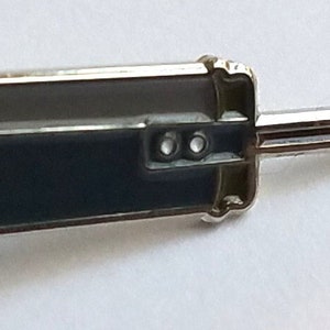 May include: A silver pin shaped like a sword with a dark gray blade and a silver handle. The pin has a back clasp.