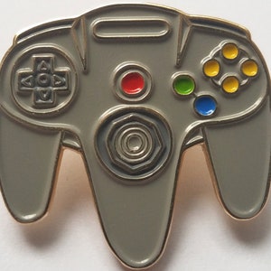 May include: A gray Nintendo 64 controller with a black and gray center button, red, green, blue, and yellow buttons, and a gray directional pad.