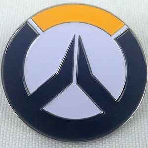 May include: A round, black and white Overwatch logo pin with a yellow accent. The logo features a stylized 'V' shape with a white center.
