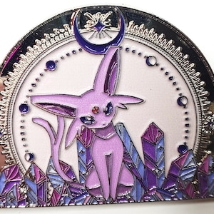 May include: A silver and purple enamel pin featuring a purple and pink Pokemon character, known as Espeon, sitting on a bed of purple crystals. A crescent moon with a star is above the character.