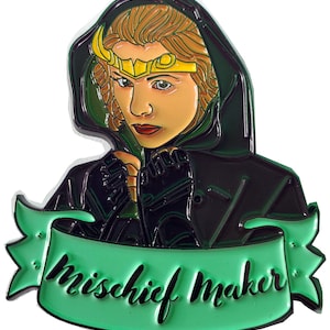 May include: A green and black enamel pin featuring a cartoon depiction of Loki, a character from the Marvel universe. The pin has a green banner with the text "mischief maker" in black.