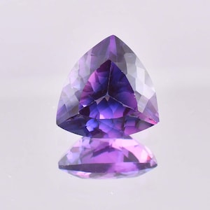 May include: A triangular cut amethyst gemstone with a purple and blue hue. The gemstone is faceted and has a high polish.