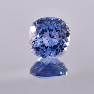 May include: A cushion-cut sapphire gemstone with a deep blue color. The gemstone is faceted and has a high degree of brilliance.