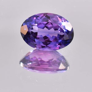 Könnte beinhalten: Ein ovaler, facettierter Edelstein in Violett. Der Edelstein reflektiert Licht und hat einen leichten rosafarbenen Farbton.