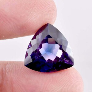 May include: A triangular faceted gemstone with a purple and blue color gradient. The gemstone is cut in a triangular shape and has a high polish.