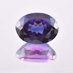 May include: A deep purple oval gemstone with a faceted cut. The gemstone is reflecting light, showing a purple and blue hue.