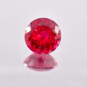 May include: A vibrant red gemstone with a round cut and a faceted surface.