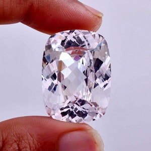 May include: A large, clear, faceted, cushion-cut gemstone with a pale pink hue.