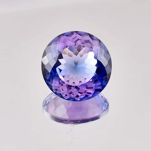 May include: A round, faceted gemstone with a purple to blue colour gradient. The gemstone is reflecting light, creating a sparkling effect.