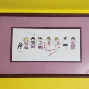 May include: A framed print of a children's illustration featuring seven children sitting on toilets, with a dog and a potted plant. The print is on a pink background with a white border and the text "We all sing our song".