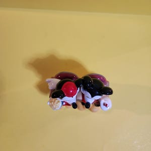 Pu&ograve; includere: Un paio di statuette di orche in ceramica, una con una palla rossa sulla testa e l'altra con una testa nera. Le orche sono nere e bianche con accenti rossi e bianchi. Sono appoggiate su una base rossa e viola.