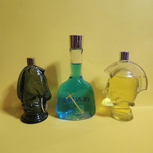 May include: Three decorative perfume bottles on a yellow background. The bottles are shaped like a knight's helmet, a horse head, and a Roman soldier's head. The bottles contain blue and yellow liquid and have silver caps.