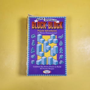 May include: A rectangular game box for Block by Block, featuring a purple background with light blue 3D block shapes. The text reads Super Spatiality! Block by Block, Puzzle Adventures in Three Dimensions! and Combine the Seven Pieces to Build 60 Puzzle Shapes.