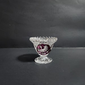 May include: A clear glass vase with a cut crystal design and a purple floral pattern. The vase has a round base and a wide mouth.