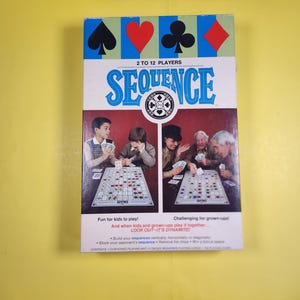 May include: A rectangular board game box for Sequence featuring the title in blue text, a circular logo, and two photographic panels showing people playing the game. The top border displays black and red card suit symbols on blue and green panels.