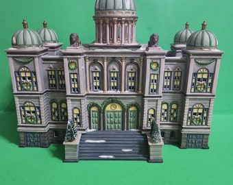 May include: A detailed miniature model of a building with a green roof and white trim. The building has a central dome and two smaller domes on either side. The building is decorated with wreaths and garlands.