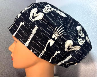Op de afbeelding: Zwarte chirurgische scrubcap met een witte skeletprint en anatomische labels. De cap bevat afbeeldingen van botten, schedels en de wervelkolom. De medische cap is ontworpen voor professionals in de gezondheidszorg.