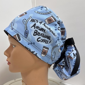 Könnte beinhalten: Blaue und schwarze OP-Mütze mit einem weißen Aufdruck, der "ABC's of Anesthesia: Airway, Breathing, Coffee!" lautet und Bilder von Kaffeetassen und medizinischen Geräten zeigt.