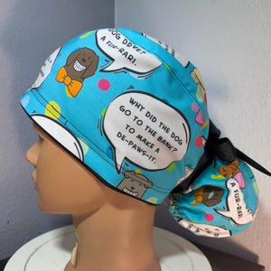 May include: A blue surgical scrub cap with a dog-themed print. The cap features cartoon dogs, speech bubbles with puns, and colorful polka dots. The text on the cap includes phrases like "Dog Dove? A Fur-rari" and "Why did the dog go to the bank to make a de-paws-it."