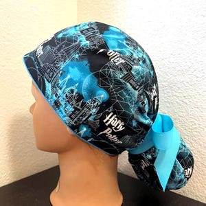 May include: A black and blue scrub cap featuring a design with the words "Harry Potter" and architectural elements. The cap has a light blue trim and a matching bow at the back. The design includes a network of lines and shapes.