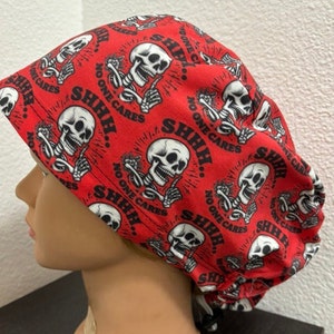 Puede incluir: Un gorro de quirófano rojo con un patrón de calavera y huesos cruzados. El gorro tiene el texto "SHHH... NO ONE CARES" repetido en toda su superficie.