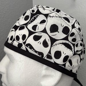 Puede incluir: Un gorro de quirófano blanco y negro con un diseño repetido de la cara de un personaje de dibujos animados. El gorro tiene una banda elástica negra.