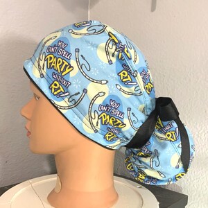 Könnte beinhalten: Eine hellblaue OP-Haube mit schwarzer Schleife. Die Haube hat ein sich wiederholendes Muster aus Musikinstrumenten-Grafiken und den Text "You can't spell PARTY without RT!"