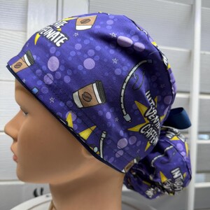 May include: A purple scrub cap featuring a repeating pattern of coffee cups, medical tubing, and yellow stars. The fabric is printed with the text "VENTILATE CAFFEINATE" in white capital letters. The cap has a gathered back with a dark blue ribbon.