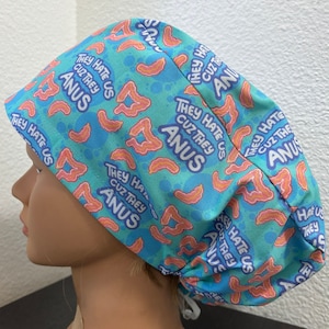 Könnte beinhalten: Eine blaue und türkisfarbene OP-Haube mit einem sich wiederholenden Muster aus rosa und orangefarbenen anatomischen Formen und dem Text "THEY HATE US CUZ THEY ANUS" in Weiß. Die Haube ist hinten gebunden.