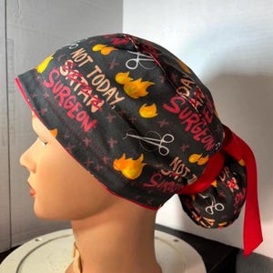 May include: Black surgical scrub cap with red trim and a red ribbon tie. The cap features the text "NOT TODAY, SATAN, SURGEON" in red and white, along with yellow flames and surgical scissors.