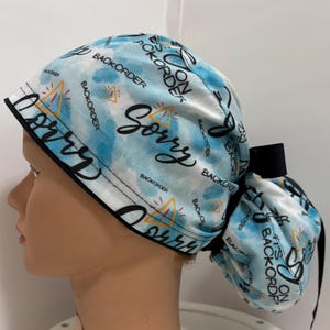 Könnte beinhalten: Eine blaue und weiße gemusterte OP-Mütze mit schwarzer Schleife. Die Mütze trägt den Text "Sorry It's On Backorder" wiederholt.