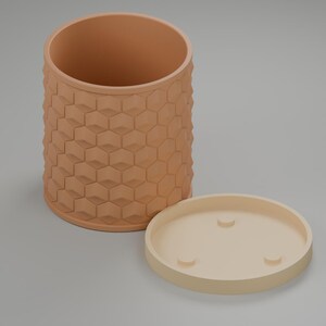 Peut inclure: Un pot de fleurs cylindrique de couleur pêche présentant un motif hexagonal en relief sur sa surface extérieure. Le pot est accompagné d'une soucoupe circulaire séparée, de couleur beige clair, dotée de trois petits pieds surélevés.
