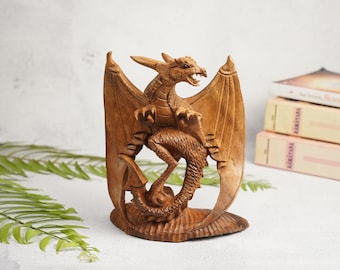 May include: A wooden dragon sculpture with outstretched wings, carved in a detailed, realistic style. The dragon is perched on a base with its tail curled around its body.